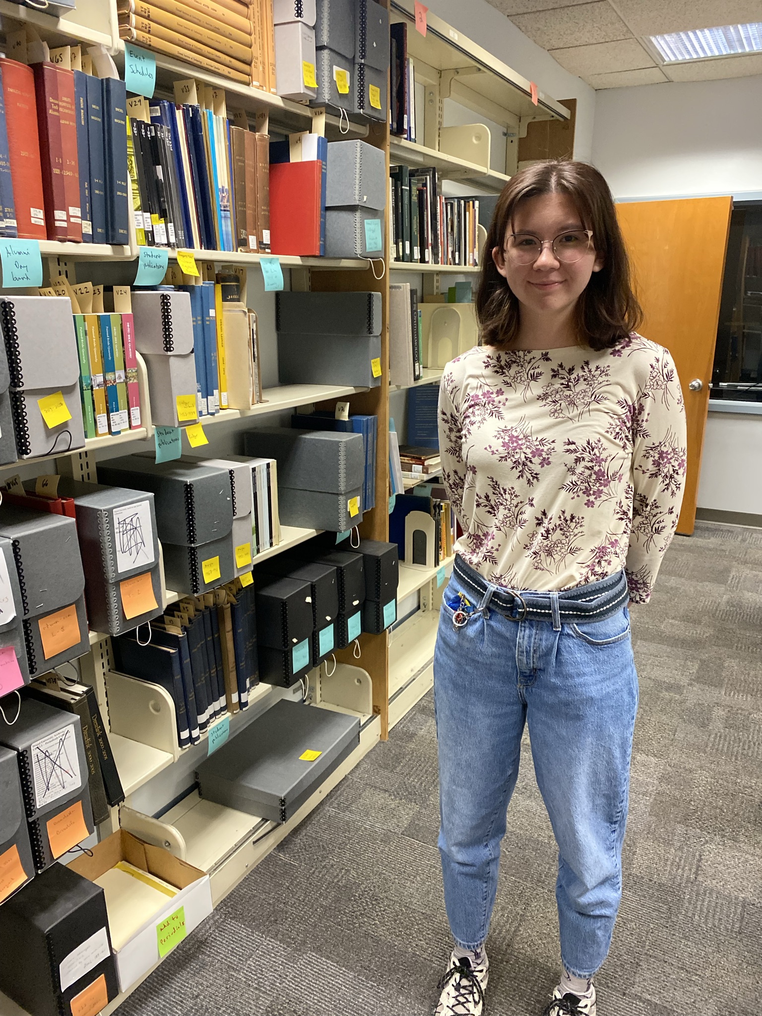 Sophia Stutte stands next to archival items on a bookshelf.